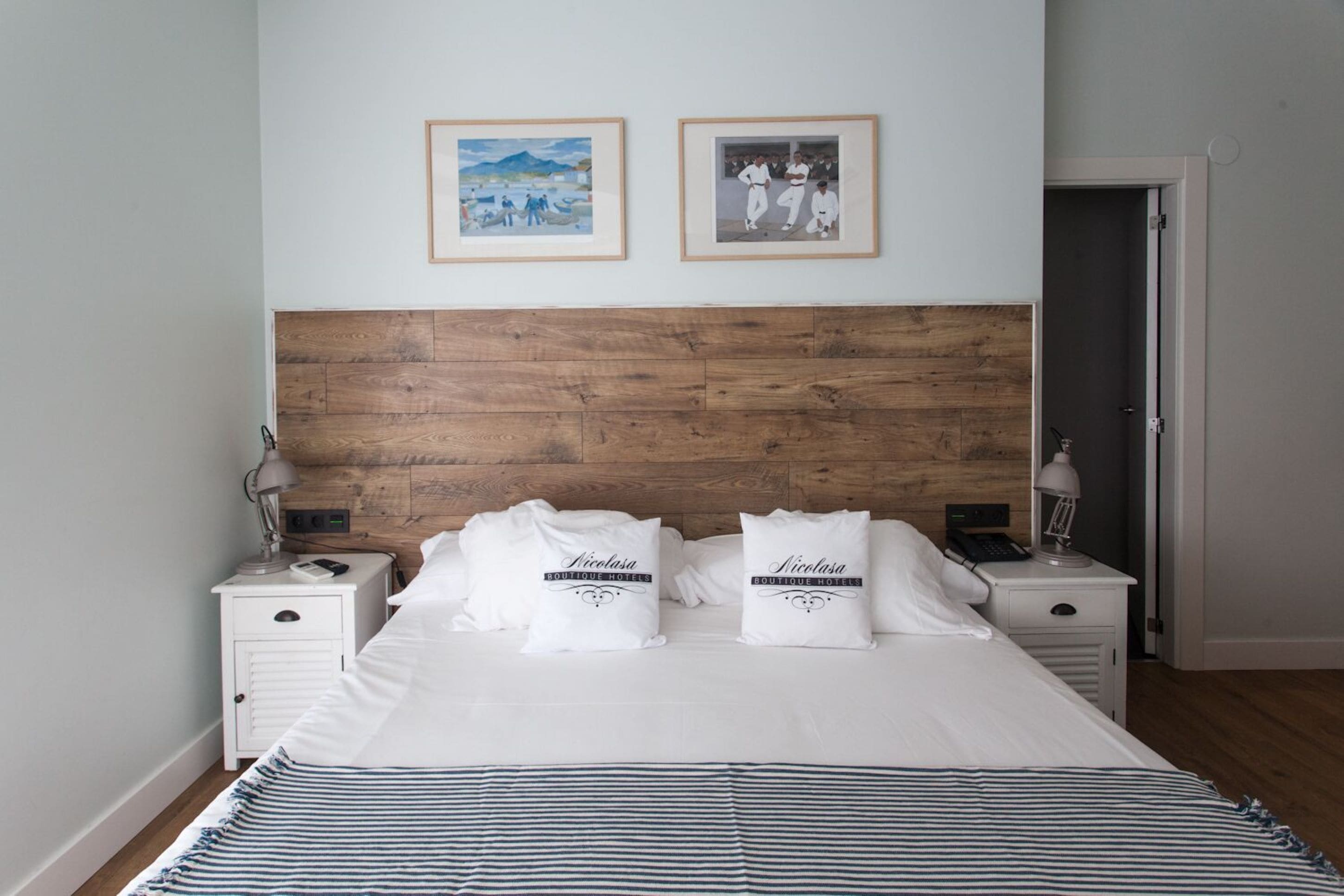 Un lit bien fait, avec deux oreillers, une tête de lit en bois et deux tables de chevet avec des lampes.