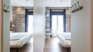 Una habitación con dos camas, una pared de piedra, televisión y ventana con cortinas.