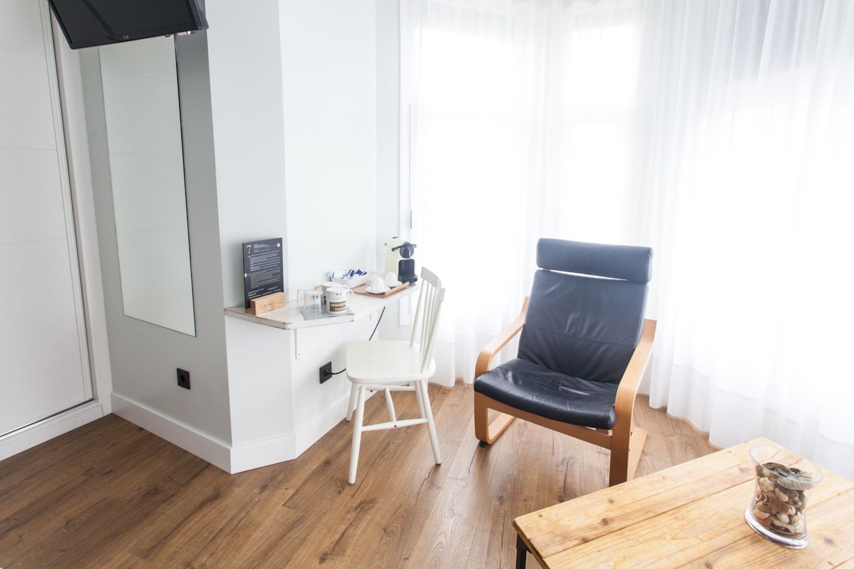 A room with a desk, a chair, a small table, and a window with curtains.