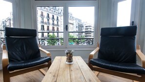 Una habitación con dos sillones de cuero negro y una mesa de madera, un jarrón con piedras, y vistas a edificios a través de una ventana.