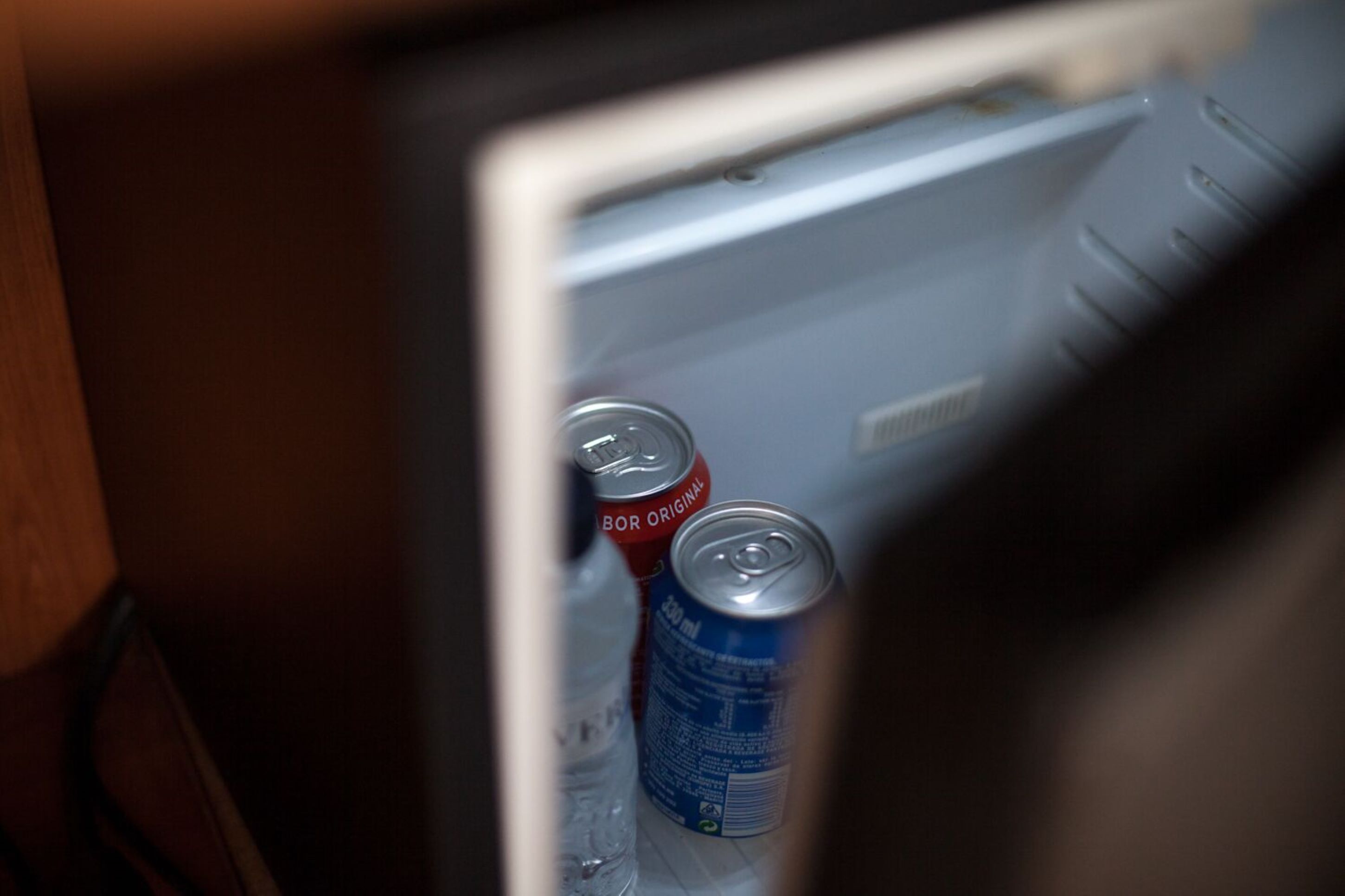 A refrigerator with two cans of soda and a bottle of water.