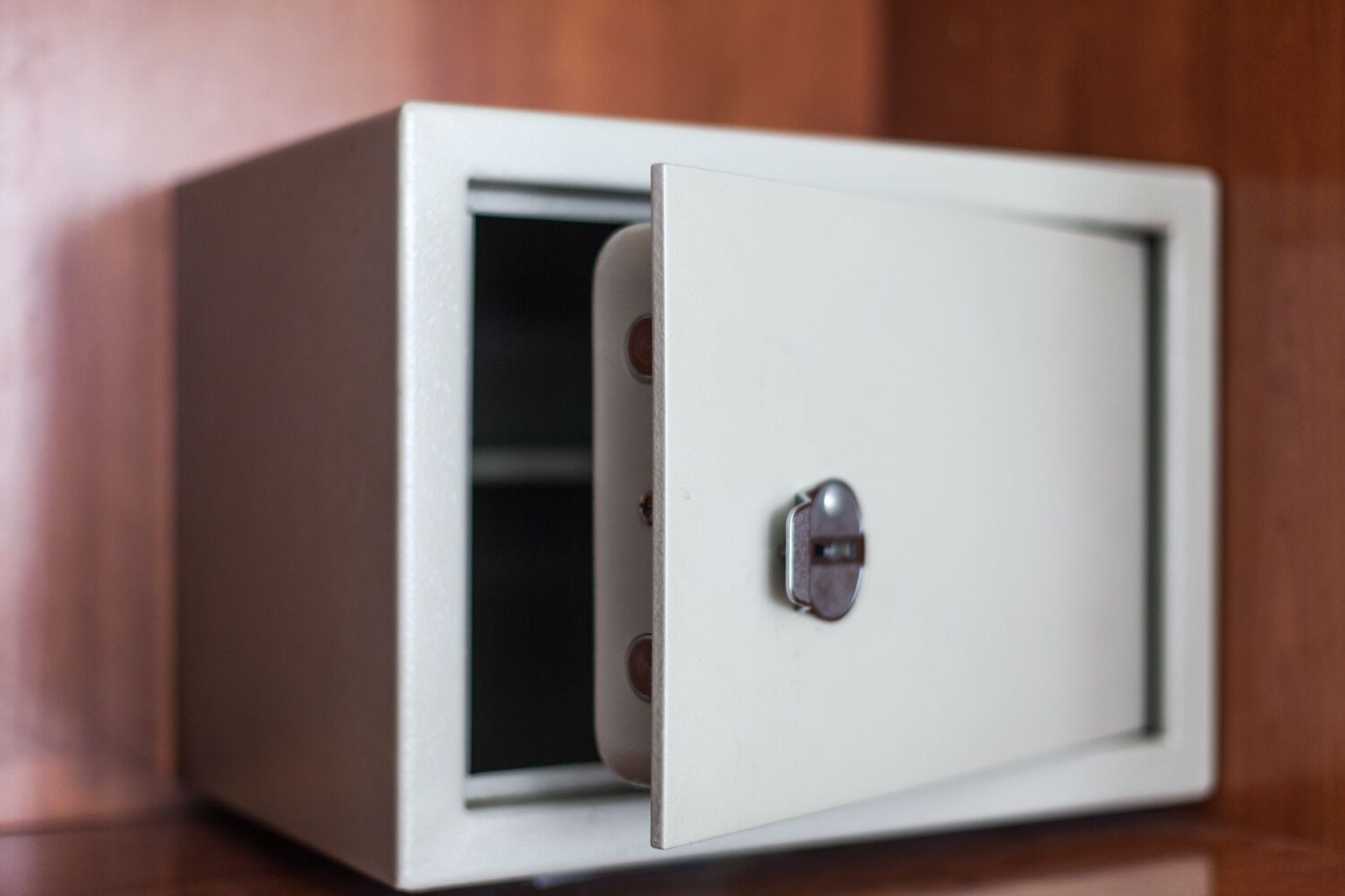 A white safe with a combination lock, placed against a wooden background.