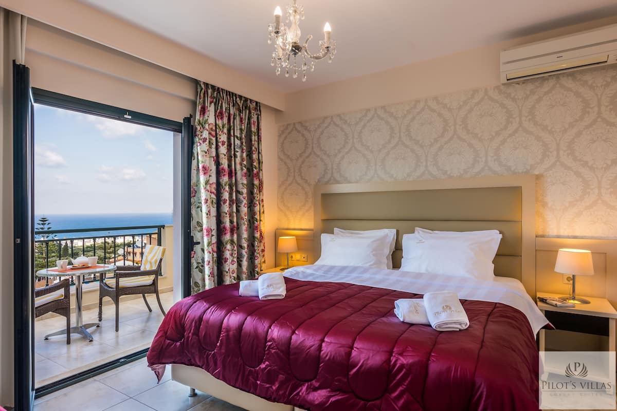 A hotel room with a large bed, a balcony with a table and chairs, and a view of the sea.