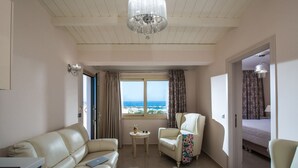 Ein Hotelzimmer mit einer Ledersofa, einem kleinen runden Tisch mit einer Pflanze, einem Sessel mit floralem Überwurf und Meerblick durch große Fenster.