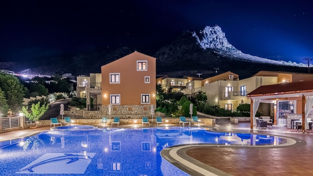 Ein Schwimmbecken mit Liegestühlen, ein Steinhaus und ein Berg im Hintergrund.