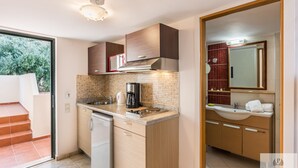 Eine moderne Küche mit Geschirrspüler, Herd und Kaffeemaschine. Ein kleines Waschbecken und ein Spiegel befinden sich darüber. Die Küche verfügt über Holzschränke und eine geflieste Spritzwand.