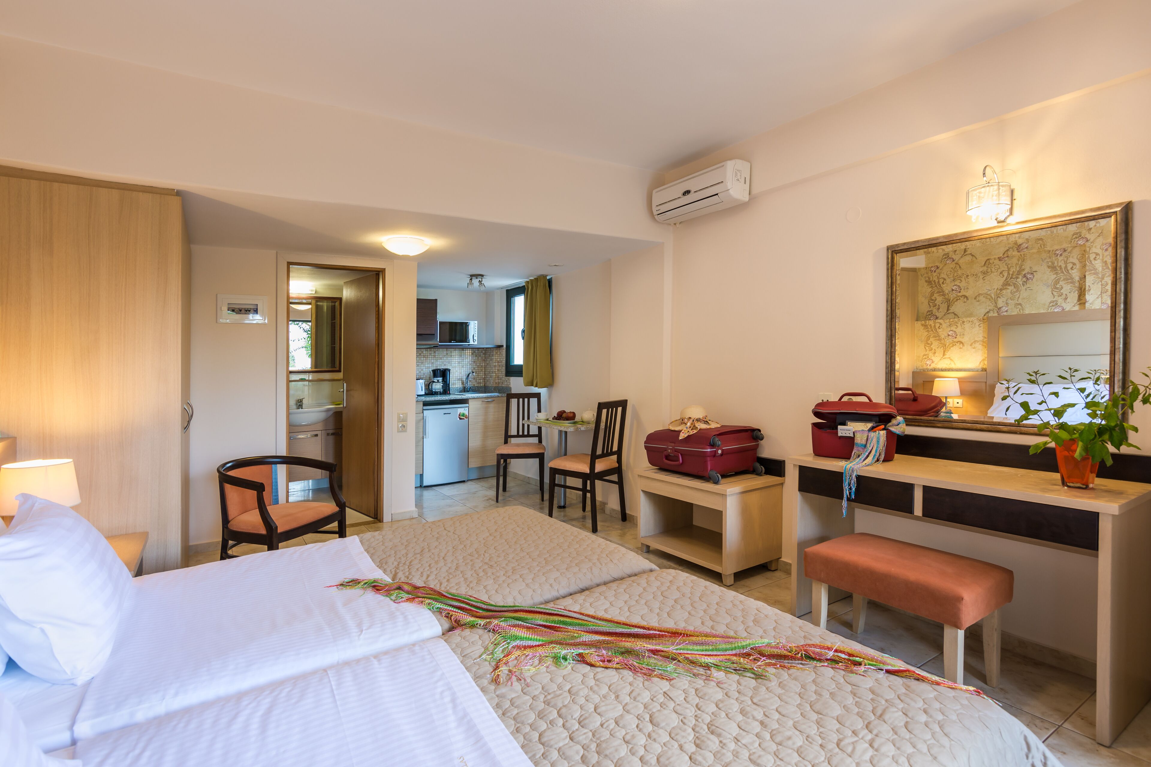 Ein Hotelzimmer mit einem Bett, einem Schreibtisch, einem Stuhl, einer Bank, einem kleinen Tisch und einer Küchenzeile im Hintergrund.