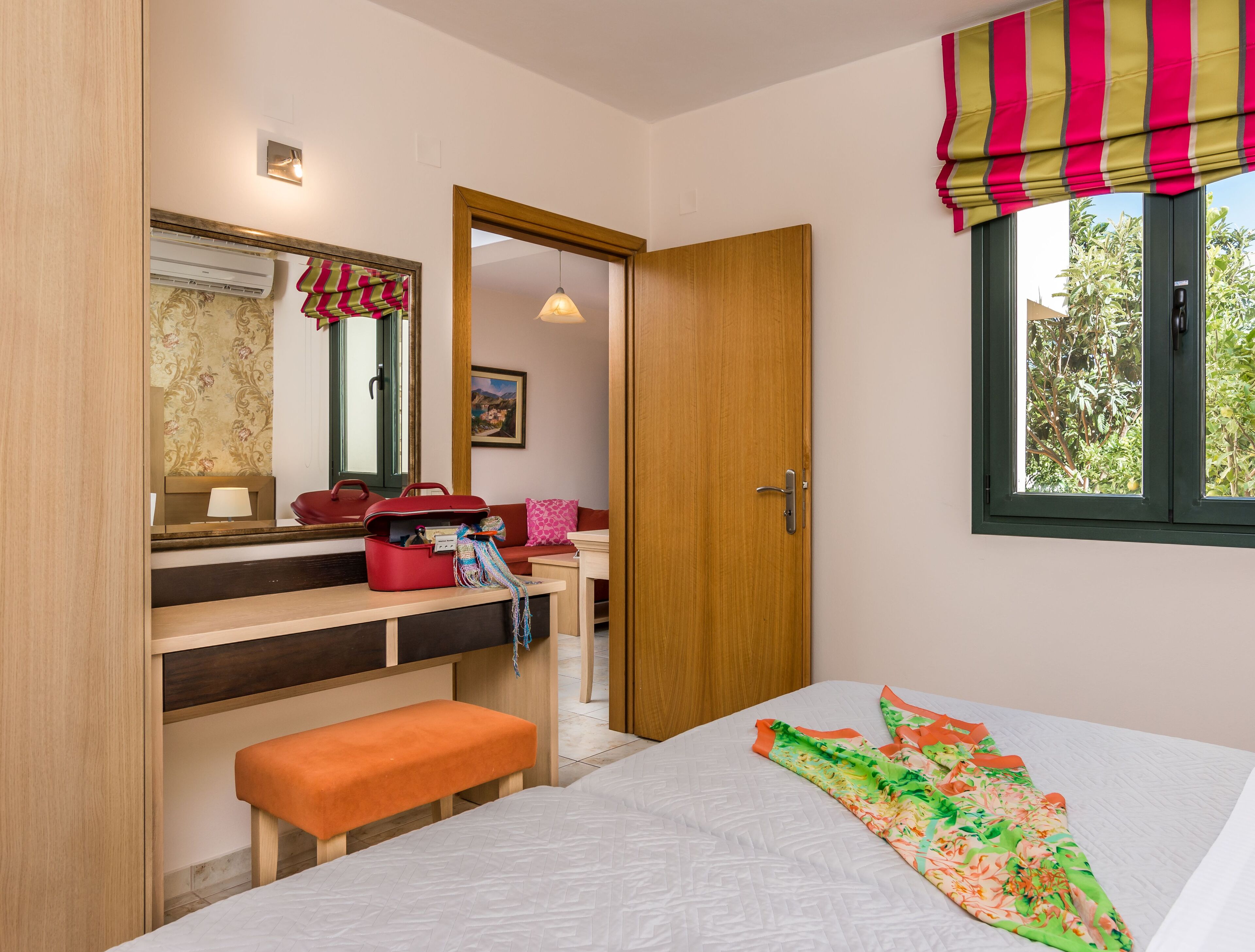 Un dormitorio con cama, banca, cómoda, espejo y ventana con cortinas.