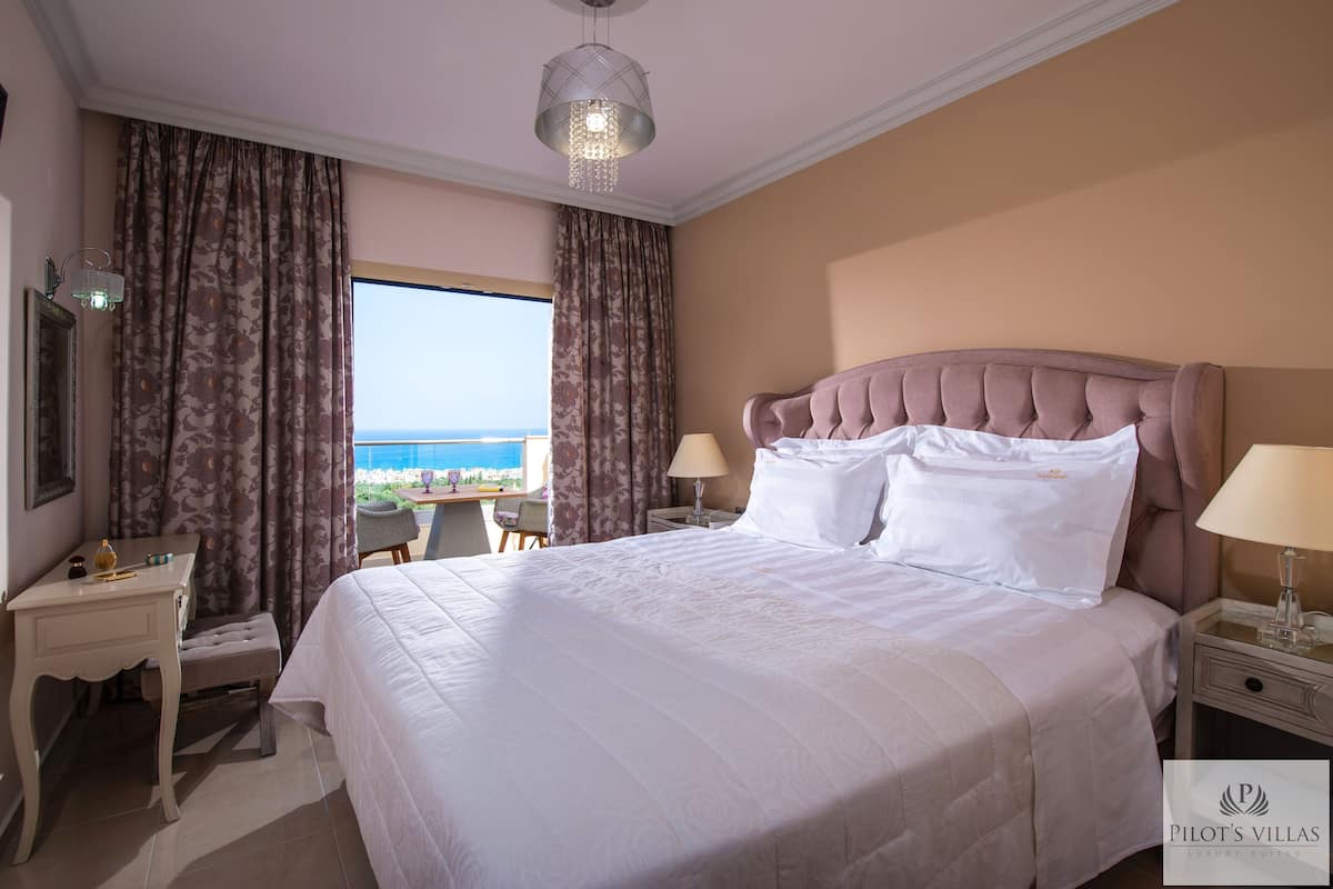 A hotel room with a large bed, a desk, a chair, and a view of the sea.