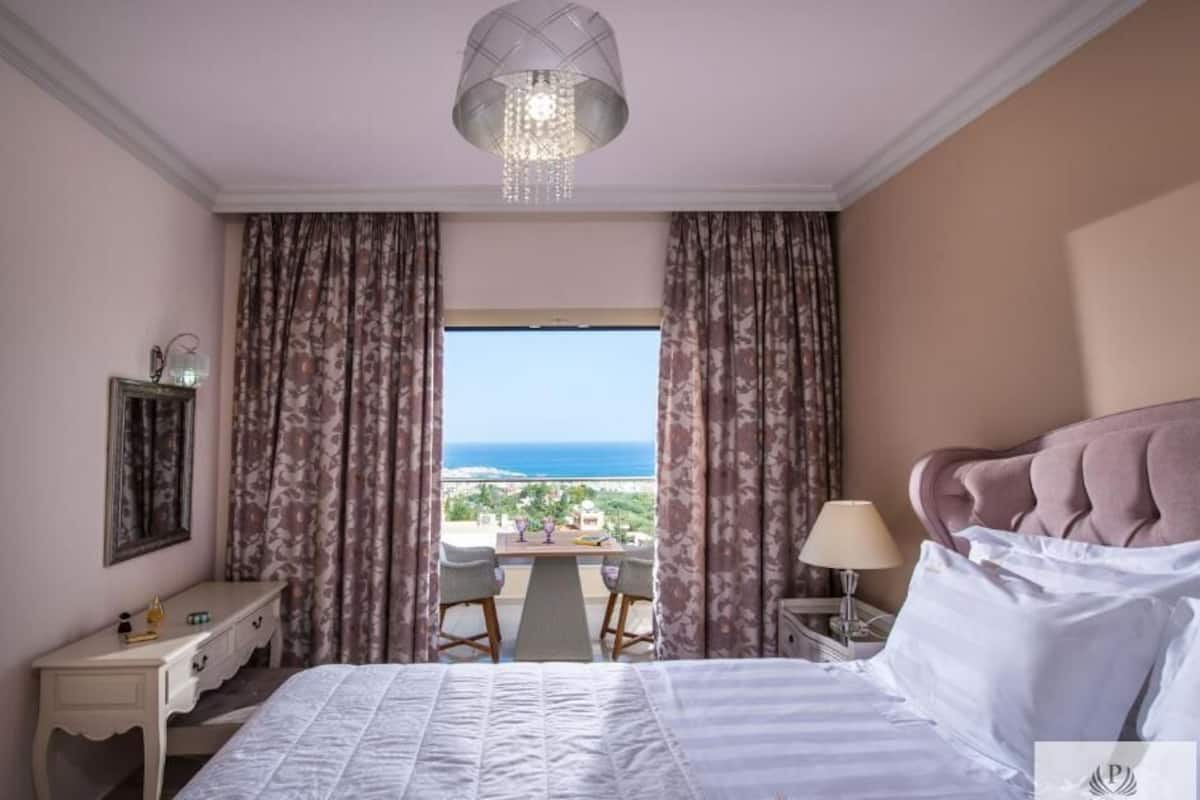 A hotel room with a bed, a desk, a chair, a lamp, and a view of the ocean.