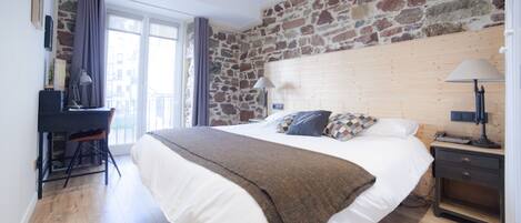 A bedroom with a large bed, a desk, a chair, a nightstand, and a stone wall.