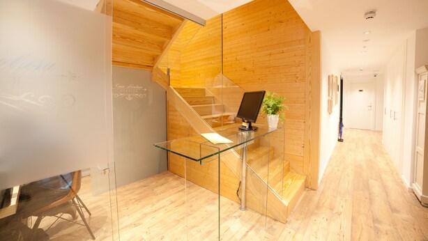 Un interior moderno con una escalera de madera, un escritorio de vidrio y una pizarra.