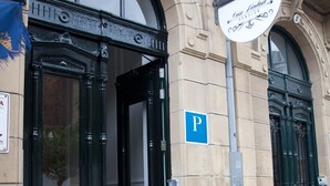 Entrada de un edificio con una puerta negra, un cartel encima y un letrero de estacionamiento azul.