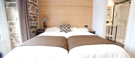 A double bed with a wooden headboard, a stone wall, and a bathroom with a glass shower.