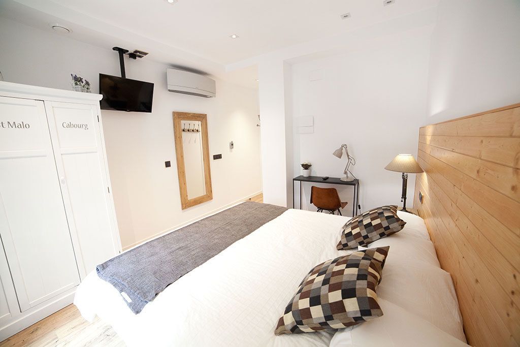Una camera da letto con un letto, una testiera in legno, una scrivania con una sedia, una lampada e un televisore fissato al muro.