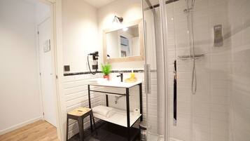A modern bathroom with a white vanity, a mirror, a shower, and a small stool.