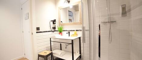 A modern bathroom with a white vanity, a mirror, a shower, and a small stool.