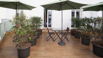 Een terras met een tafel en stoelen, omringd door potplanten en parasols.