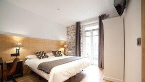 Un dormitorio con cabecera de madera, cama con ropa de cama blanca, escritorio con silla y pared de acento de piedra.