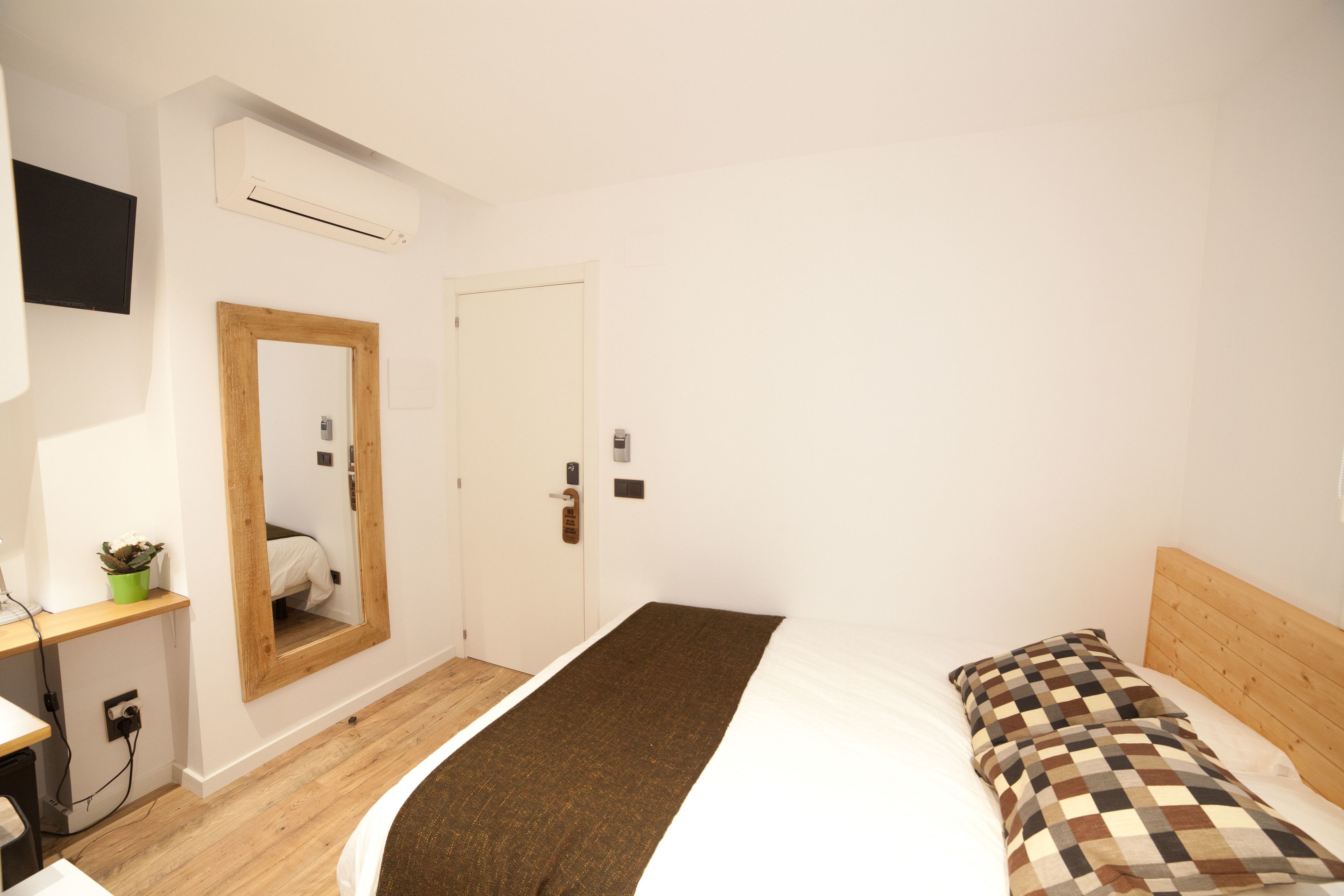 A bedroom with a bed, a wooden headboard, a mirror, a door, and a wall-mounted air conditioner.