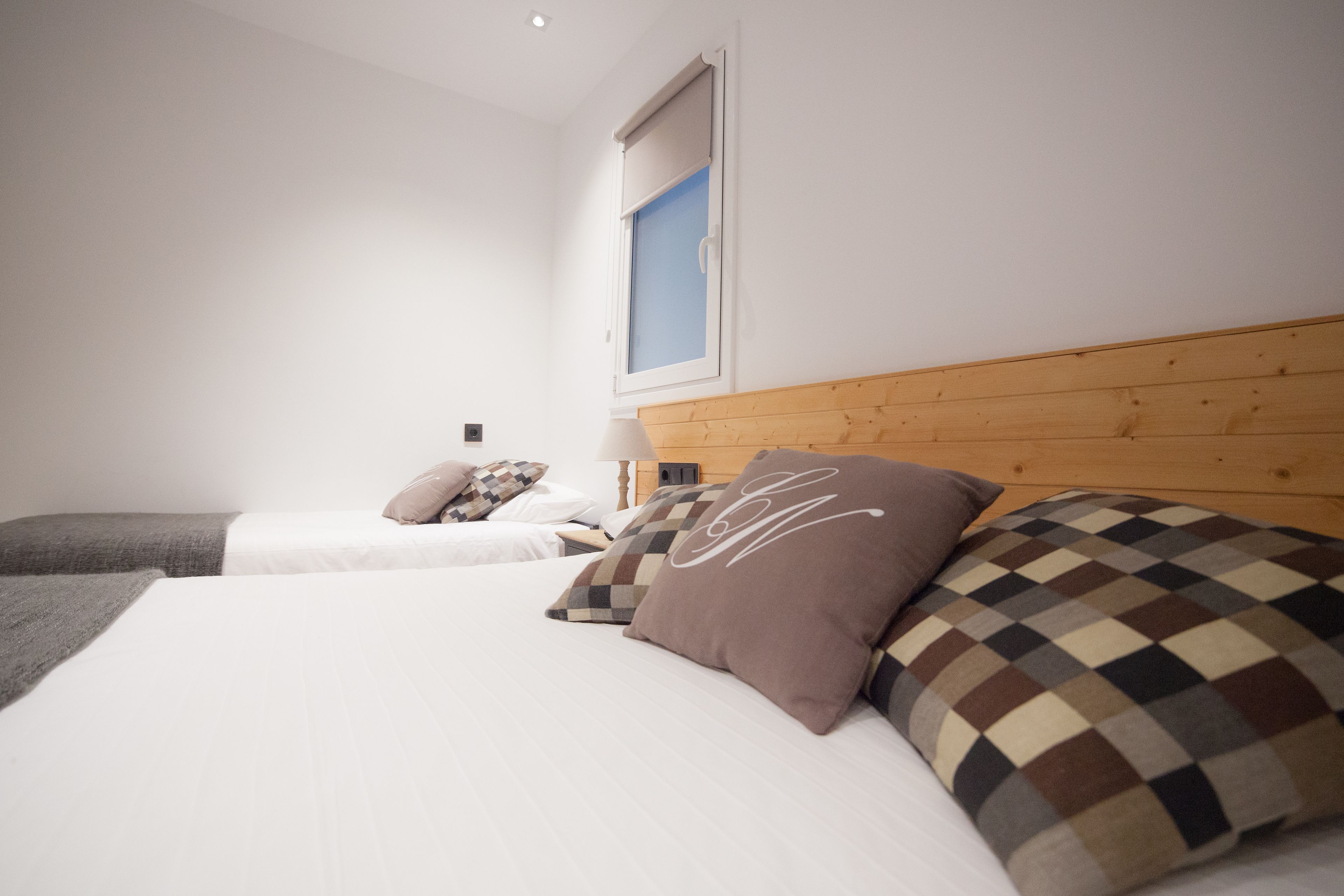 Une chambre avec deux lits, une tête de lit en bois et une fenêtre avec des stores.