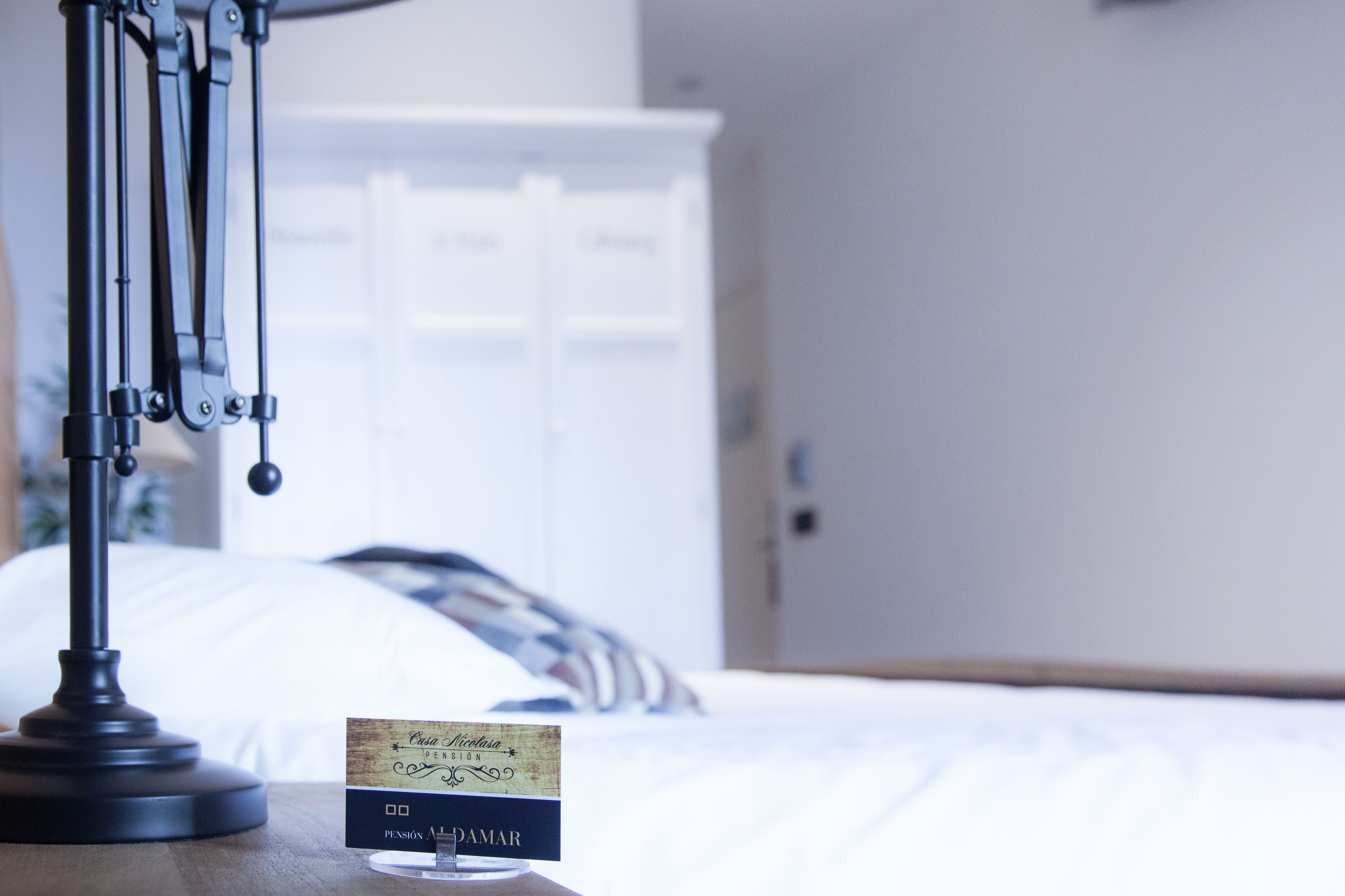 A bed with a white headboard, a bedside table with a lamp, and a sign with the name "Crispina".