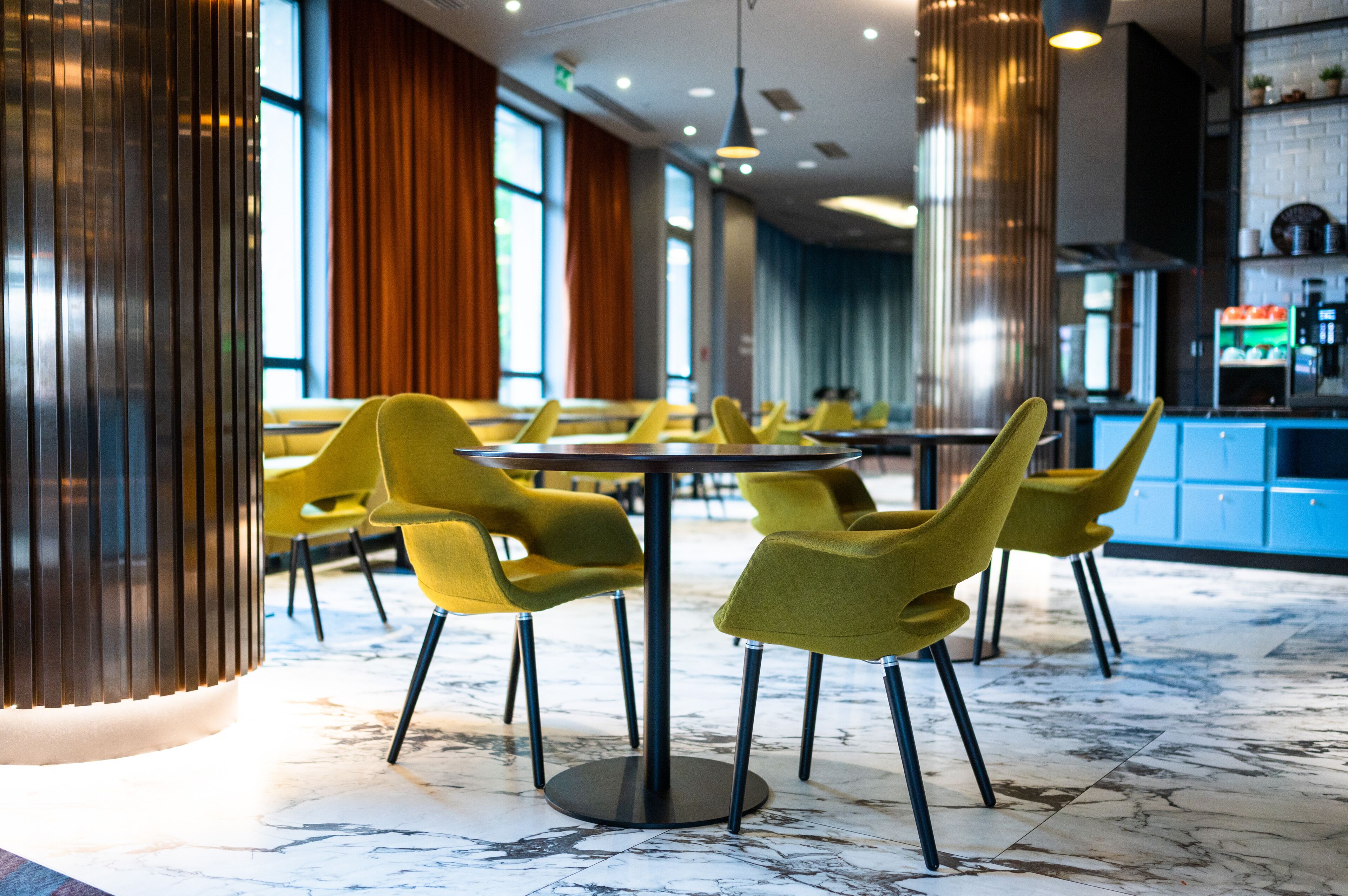 A modern restaurant with yellow chairs, marble flooring, and large windows.
