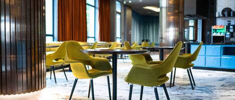 A modern restaurant with yellow chairs, marble flooring, and large windows.