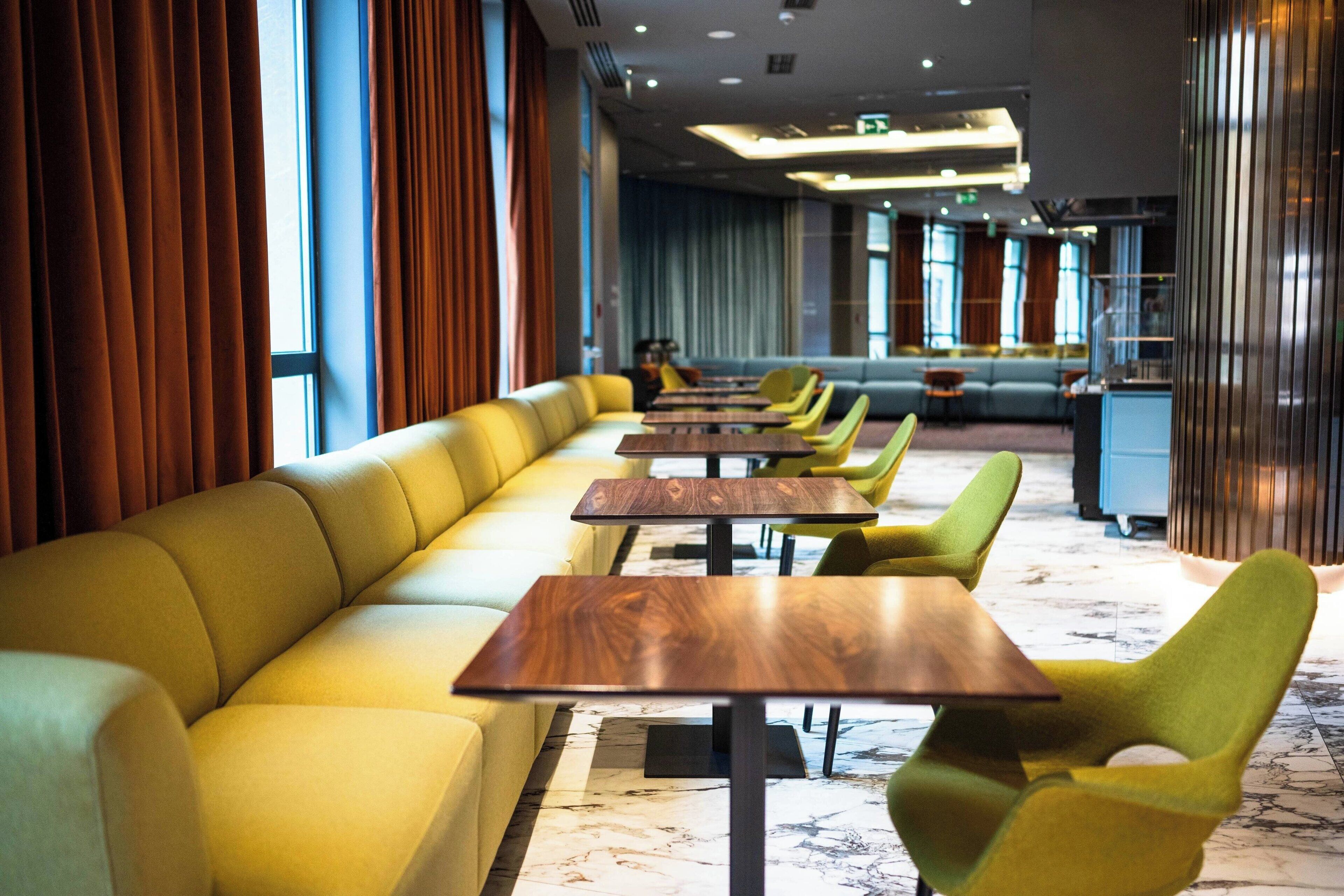 Uma sala de jantar moderna com sofás amarelos e cadeiras verdes, mesas de madeira e piso de mármore.
