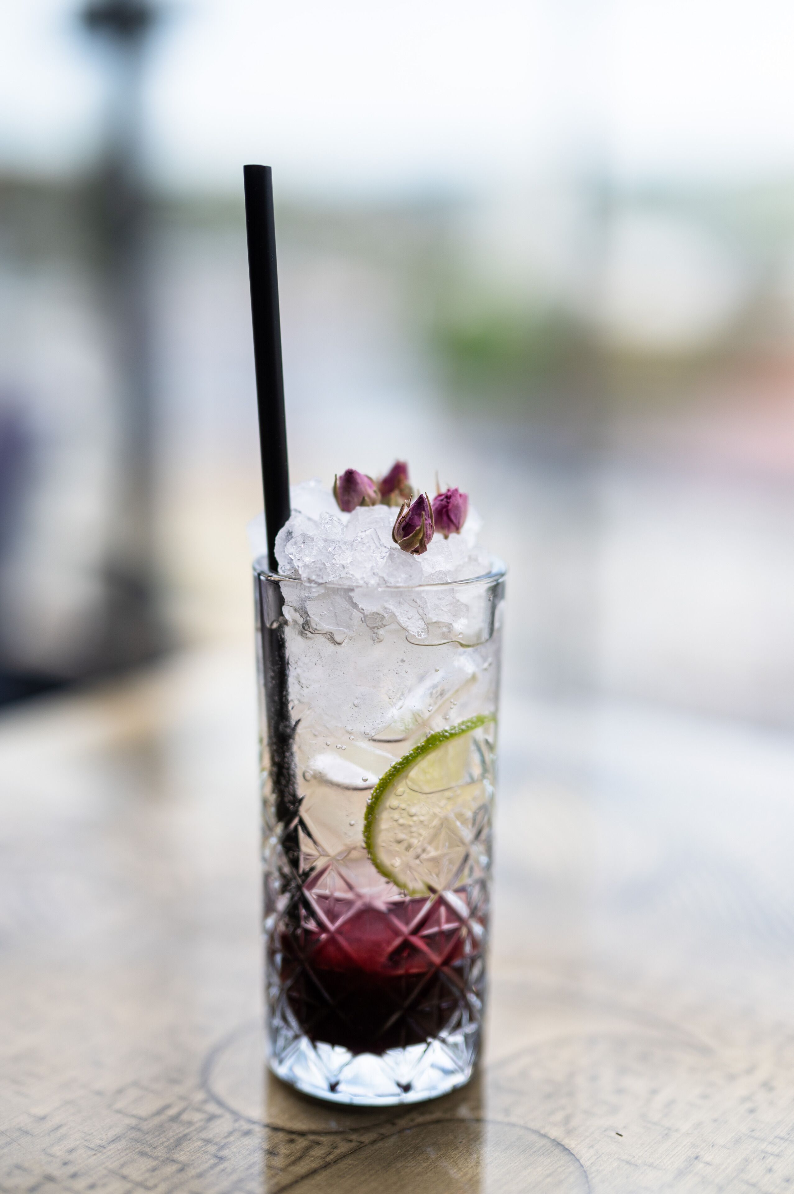 A clear glass with ice, a lime wedge, and a straw, placed on a wooden surface.
