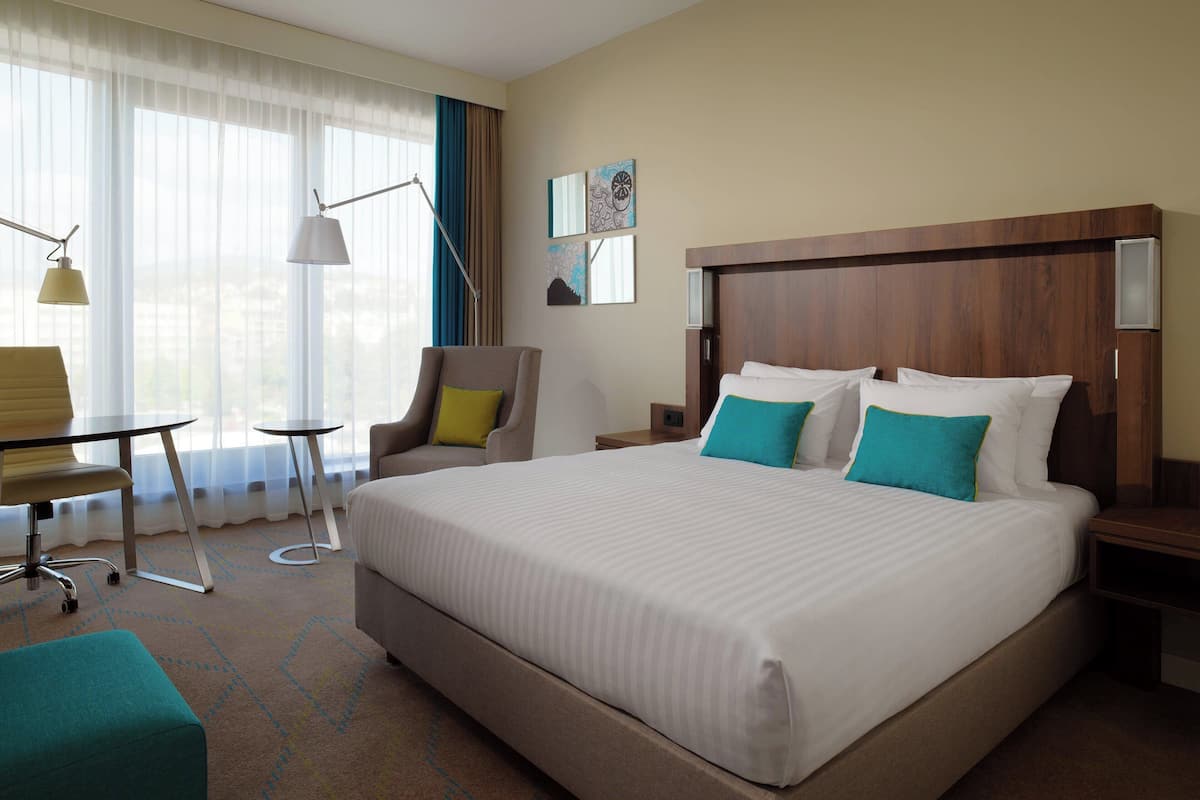 A hotel room with a large bed, a desk, a chair, and a window with curtains.