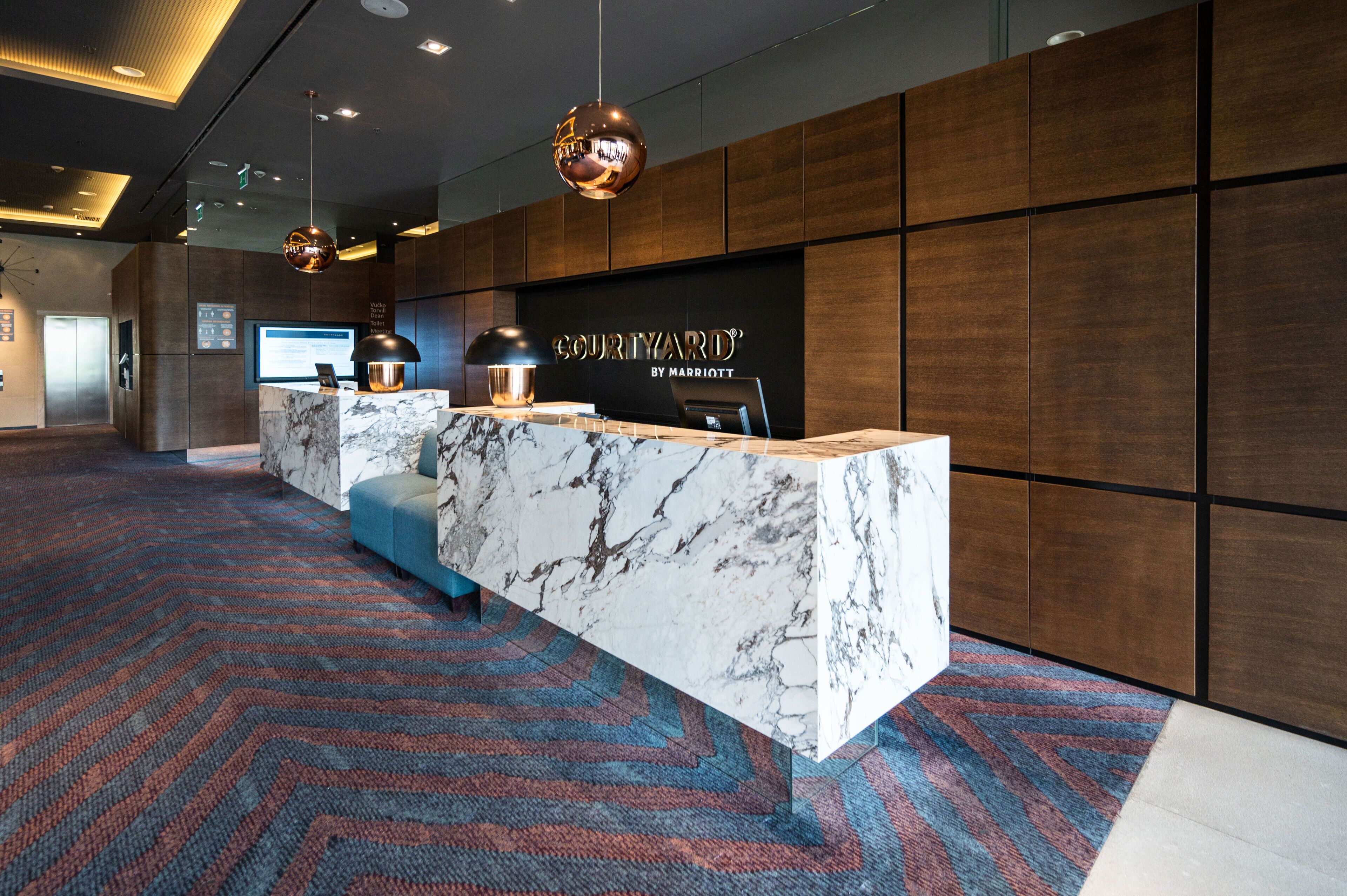 A hotel reception area with a marble counter, modern lighting, and a patterned carpet.