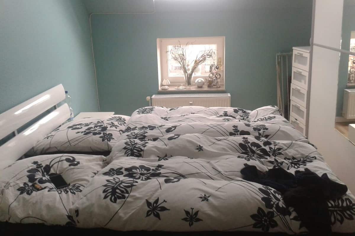 Een slaapkamer met een bed, een raam, een dressoir en een radiator.