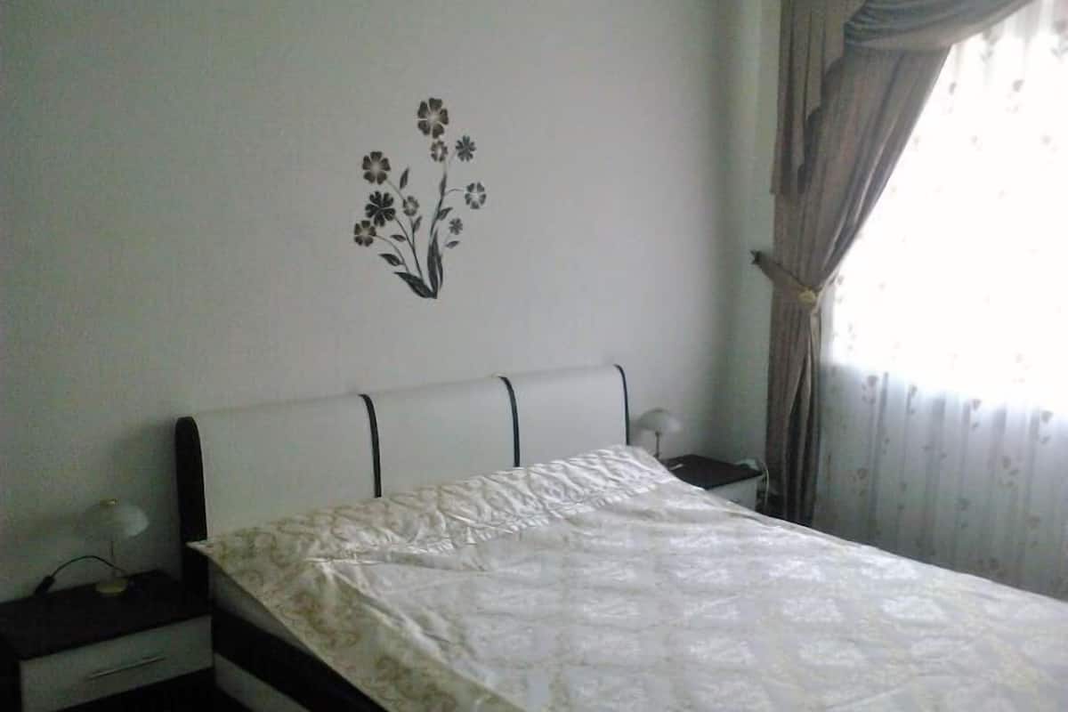 Een slaapkamer met een bed, nachtkastje, lamp en een decoratie aan de muur.