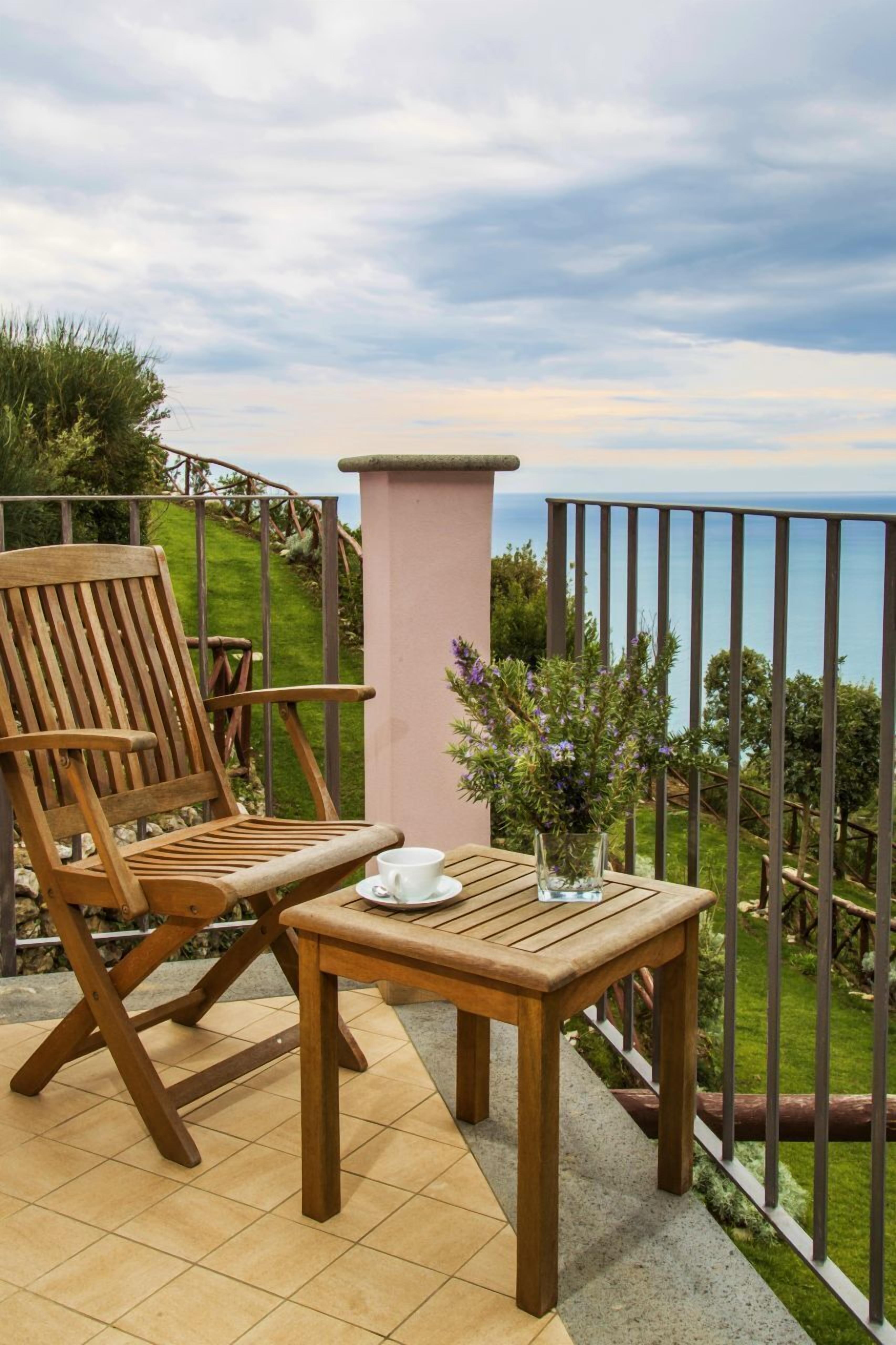 Una silla y una mesa de madera en un balcón con vista al mar.