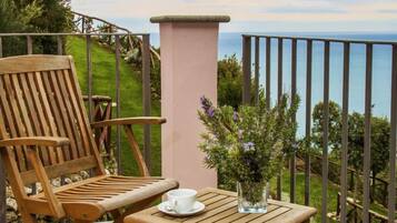 Una silla y una mesa de madera en un balcón con vista al mar.