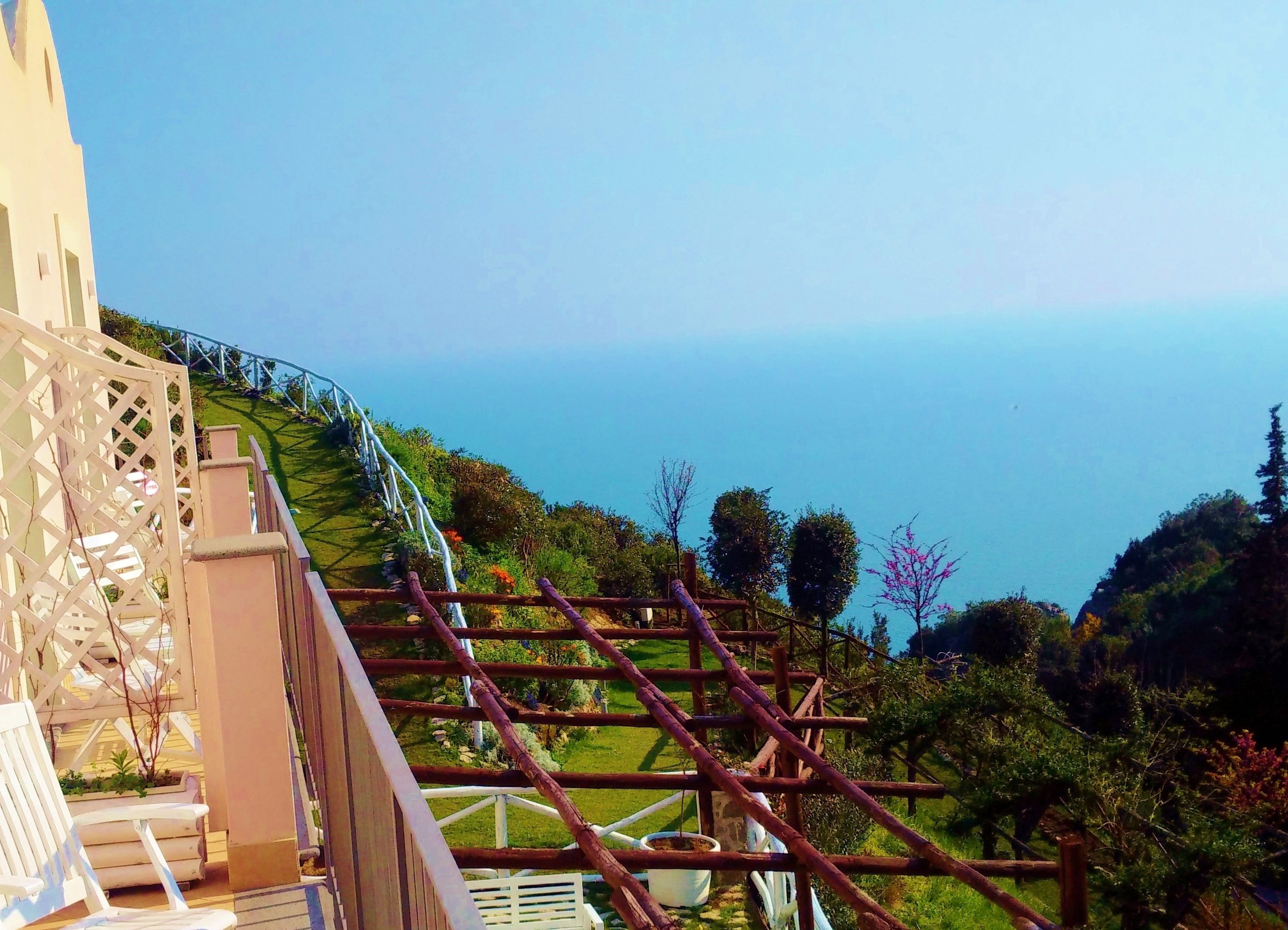 Ein Balkon mit Blick auf das Meer, einem weißen Zaun und etwas Grün.