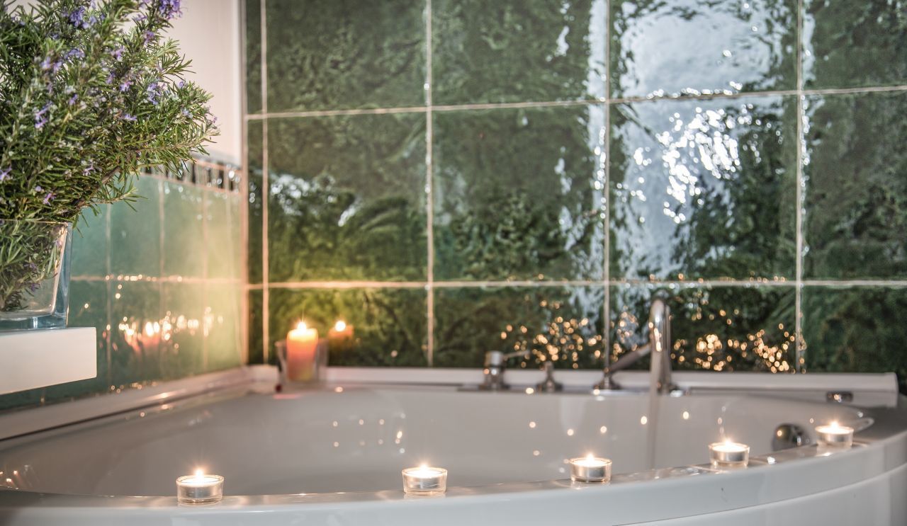 Un espace intérieur paisible, avec une grande fenêtre qui reflète la verdure, une petite fontaine d’intérieur et de nombreuses bougies créant une atmosphère chaleureuse.