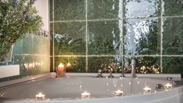 Un espace intérieur paisible, avec une grande fenêtre qui reflète la verdure, une petite fontaine d’intérieur et de nombreuses bougies créant une atmosphère chaleureuse.