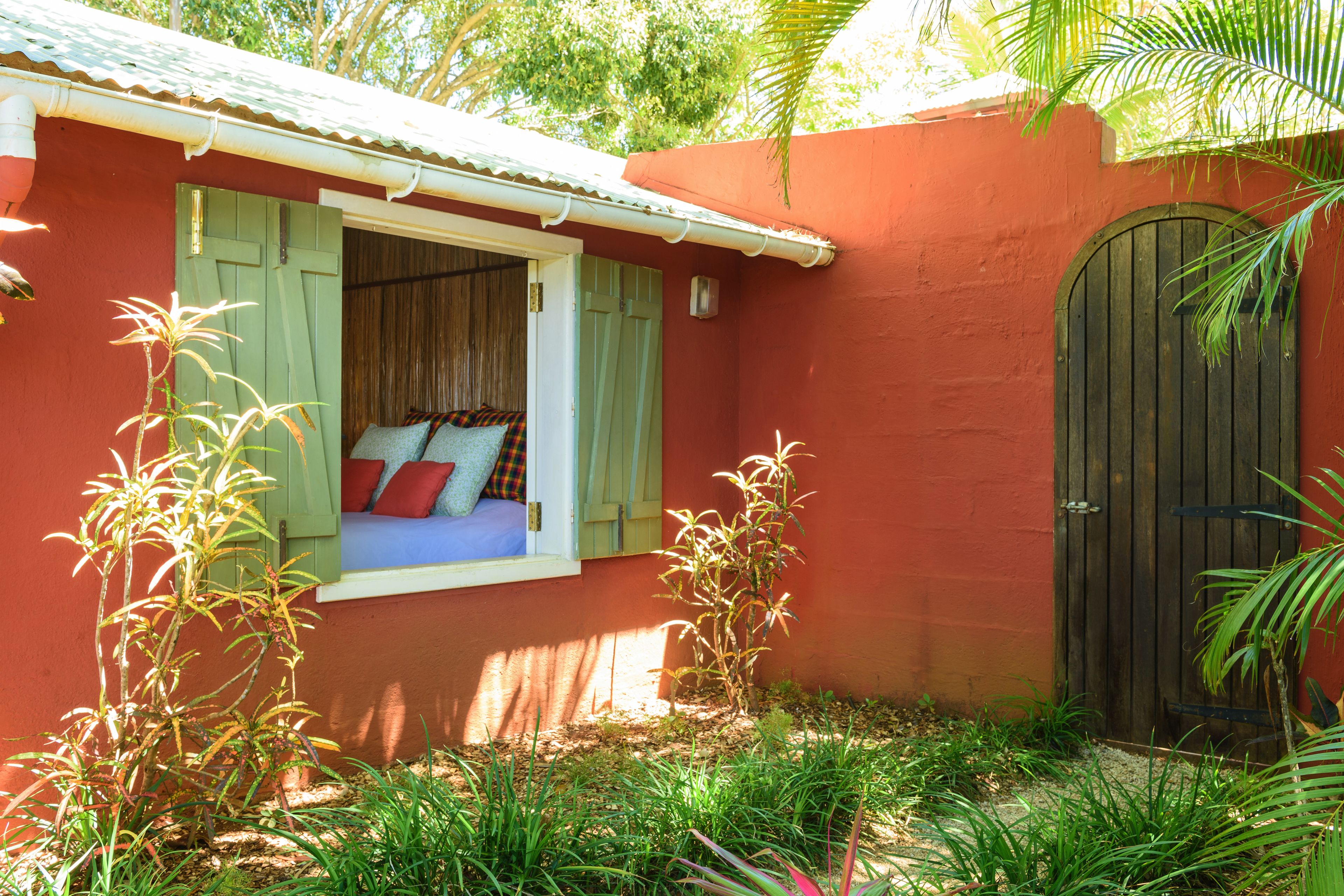 A red building with a window overlooking a bed with pillows and a view of the outdoors.