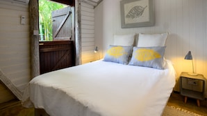 A bedroom with a bed, a nightstand, a lamp, a framed picture, and a door leading outside. - La Vieille Cheminee (Chamarel)