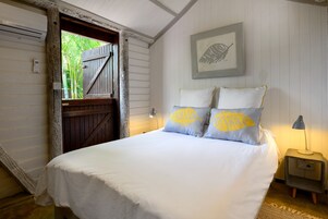 Un dormitorio con una cama, una mesita de noche, una lámpara, un cuadro enmarcado y una puerta que da al exterior.
