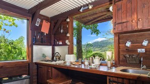 A rustic kitchen with wooden cabinets, a sink, and stools. - La Vieille Cheminee (Chamarel)