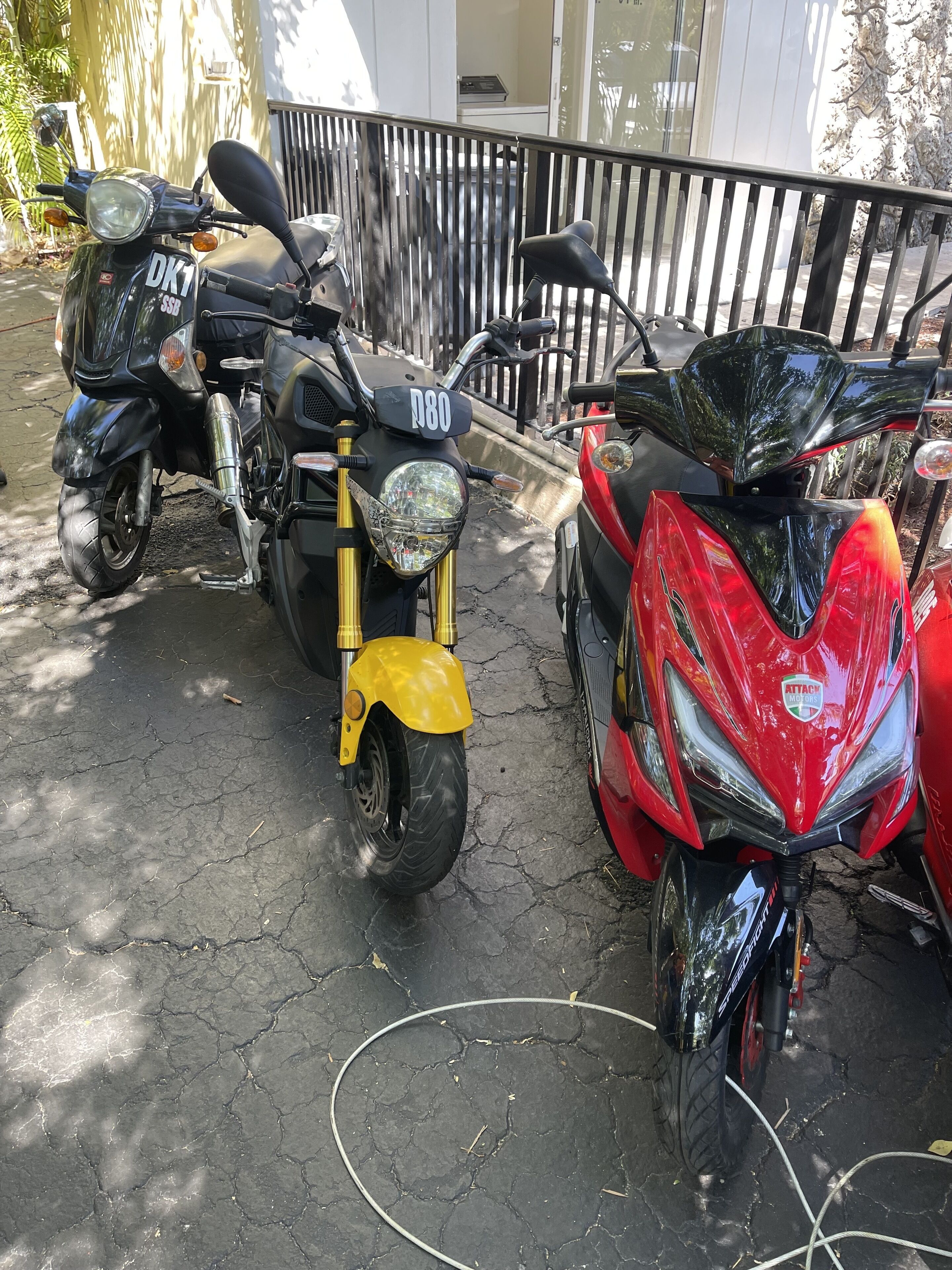 A row of motorcycles parked on a paved surface, with a metal railing and a building in the background.