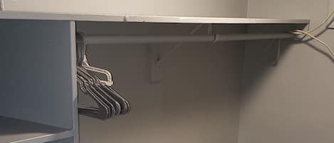 A small, enclosed storage area with a metal shelving unit, a hanging rack, and a flat shelf.