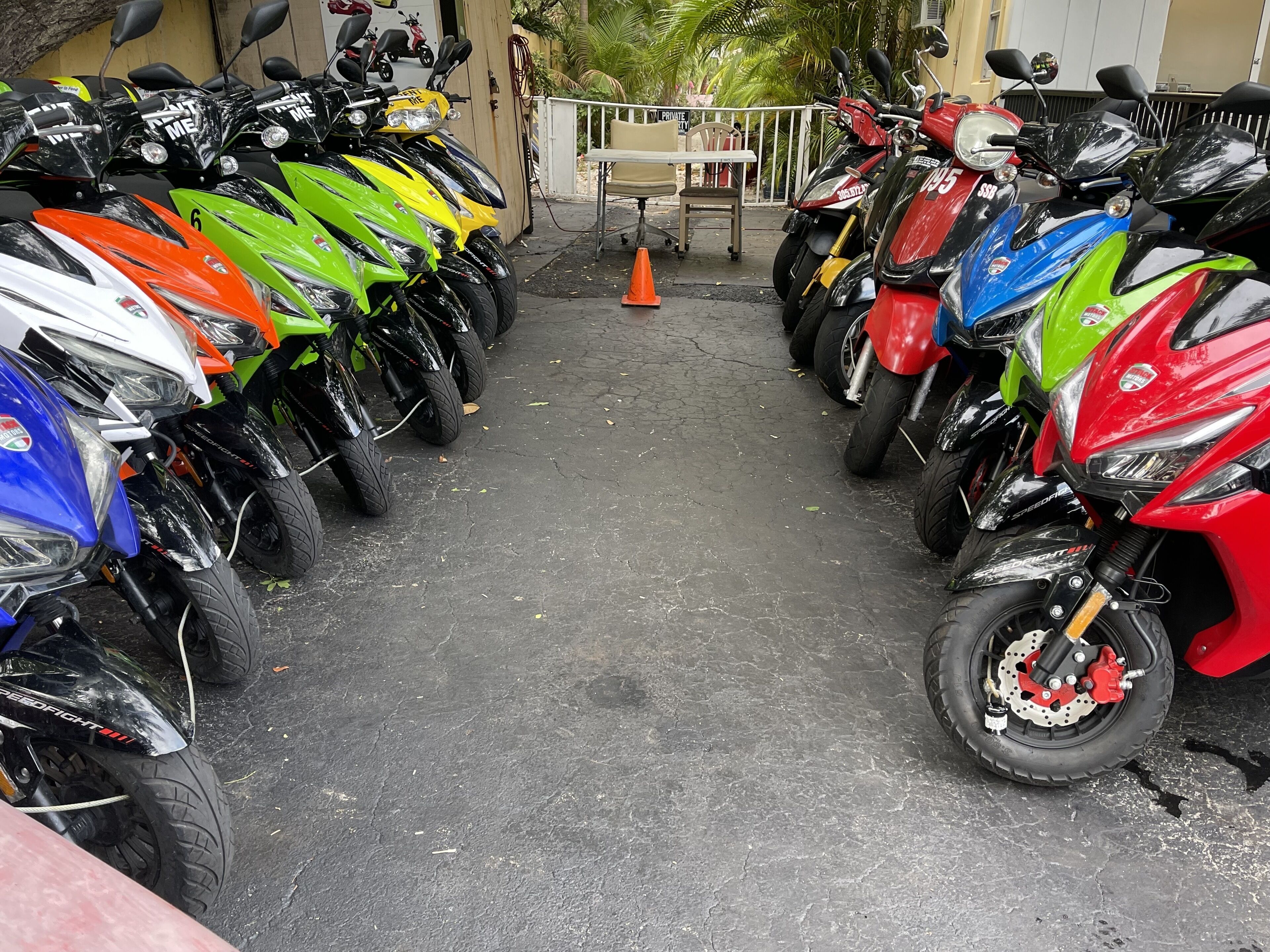 A row of motorcycles parked in a covered area with a concrete floor and a small table with chairs.
