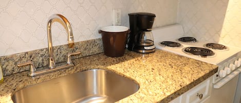 Una cocina con un lavamanos de acero inoxidable, una cafetera y una estufa.