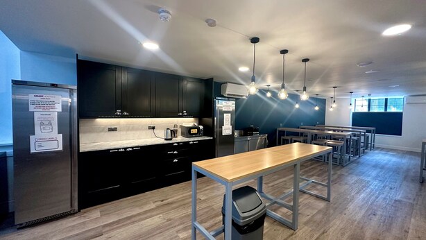 A modern kitchen with black cabinets, a stainless steel refrigerator, and a wooden dining table. - Smart Camden Inn Hostel (London)