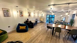 A modern living room with a sofa, a hanging chair, a dining area with a table and chairs, and a large window providing natural light. - Smart Camden Inn Hostel (London)