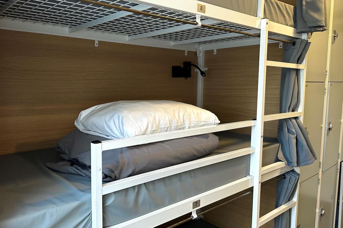 A bunk bed with a headboard, a pillow, and a blanket. There is a ventilation grille above the bed and a door with a number on it.